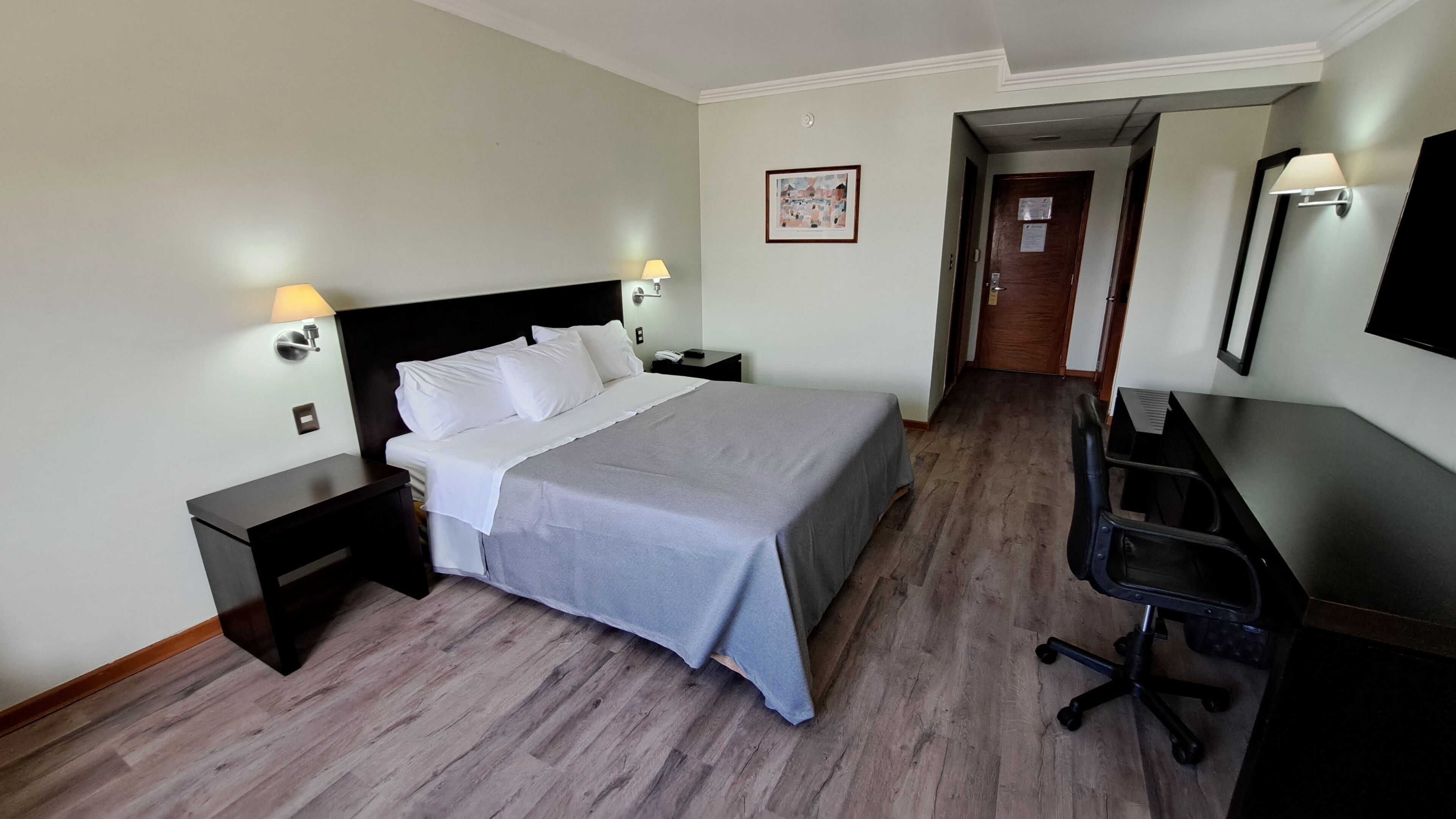 A hotel room with a bed, bedside tables, a desk, and a chair.