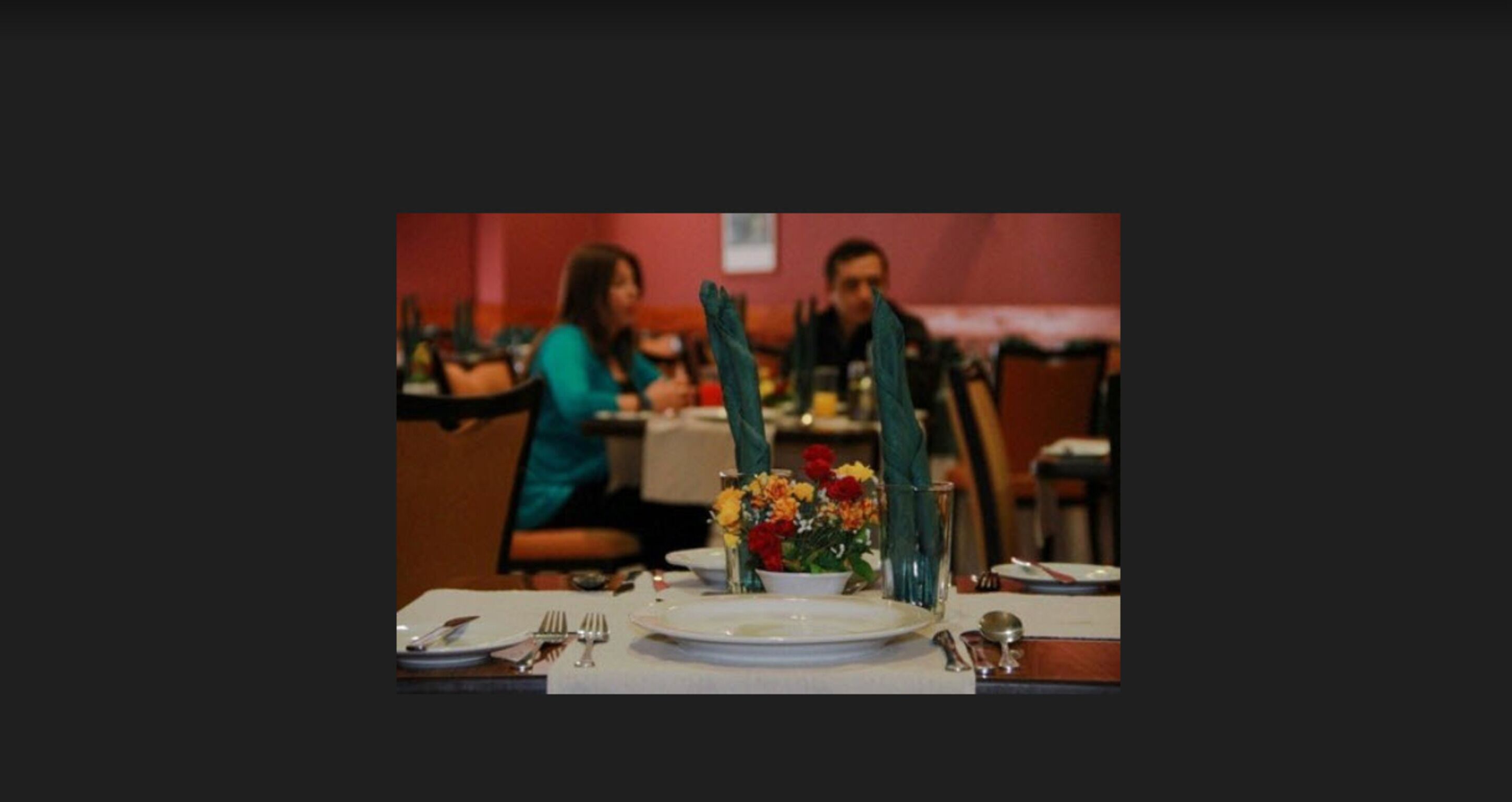 Een eettafel gedekt met borden, bestek en een vaas met bloemen.