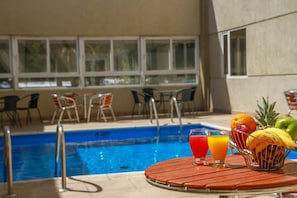 Zona de piscina con mesa, sillas y una cesta de fruta.