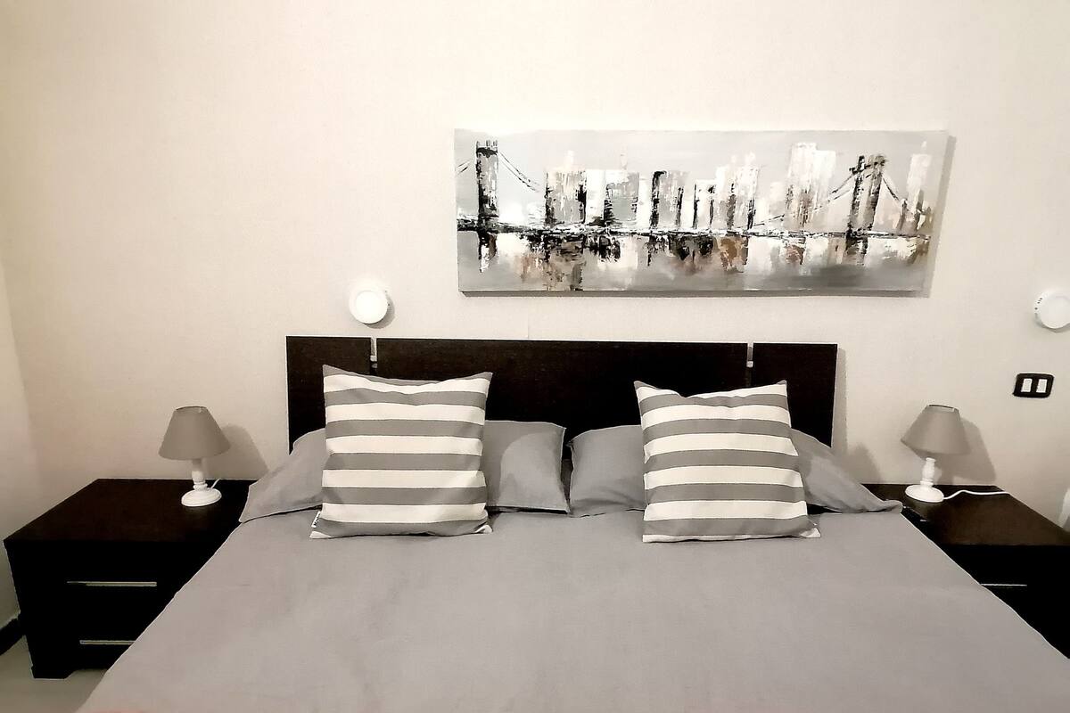 A bedroom with a large bed, two bedside tables, and a wall-mounted painting.