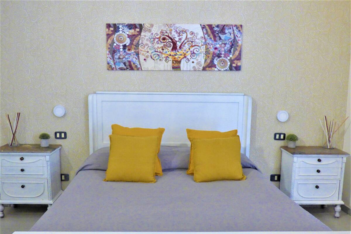 A bedroom with a bed, two nightstands, and a wall art piece.