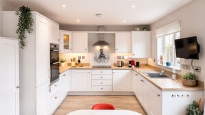A modern kitchen with white cabinets, a central island, a red chair, and a TV mounted on the wall.