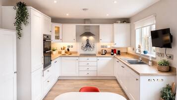 Une cuisine moderne avec des meubles blancs, un îlot central, une chaise rouge et un téléviseur fixé au mur.