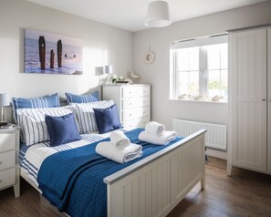 Une chambre à coucher avec un lit, une commode blanche et une fenêtre donnant sur la mer.