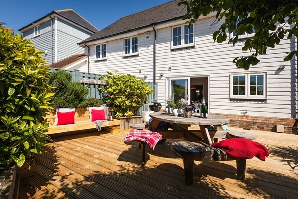 Une terrasse en bois avec une table et des chaises, entourée de verdure et bordée d’un bâtiment sur lequel on peut lire l’inscription « The Beach ».