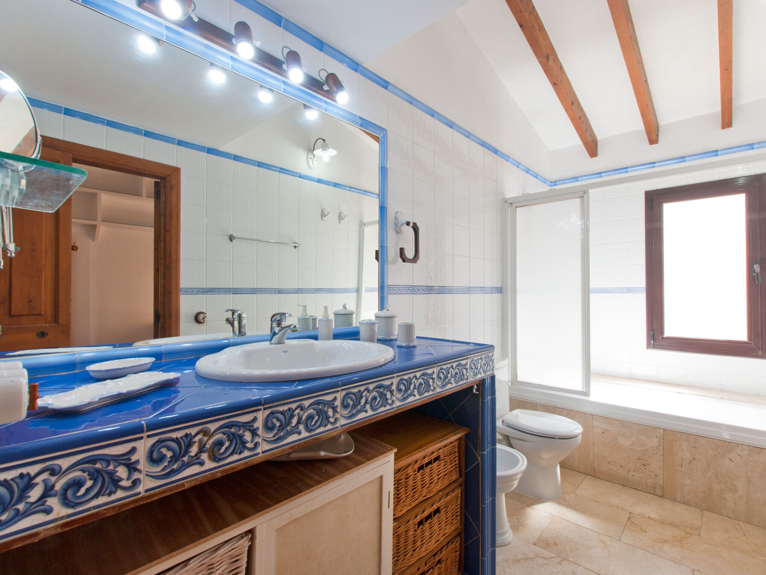 Ein Badezimmer mit einer blauen und weißen Fliesenwand, einem weißen Waschbecken, einem Spiegel und einem Fenster.