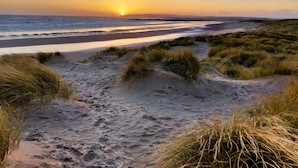 Une plage avec des dunes de sable et un coucher de soleil en arrière-plan.