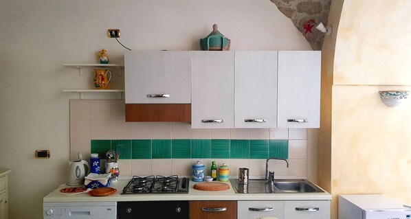 Una cocina con gabinetes blancos, estufa a gas, un lavamanos y un salpicadero de azulejos verdes.