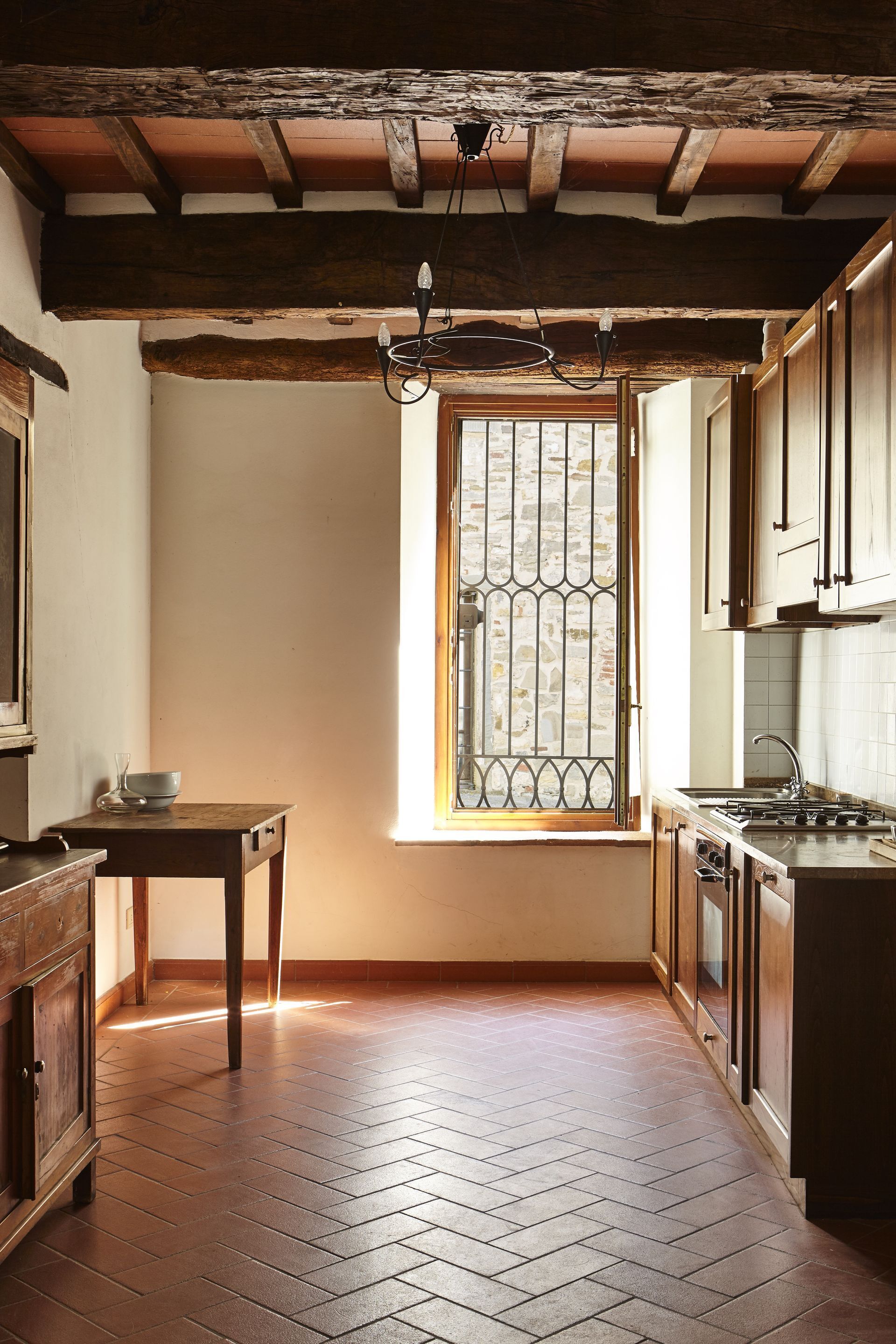 Eine Küche mit Holzausstattung, einem Fischgrätparkett, einem Fenster mit Gitter und einer hängenden Leuchte.
