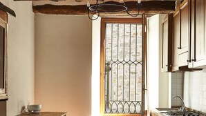 Et køkken med træskabe, fiskebensparketgulv, et vindue med tremmer og en hængende lampe.