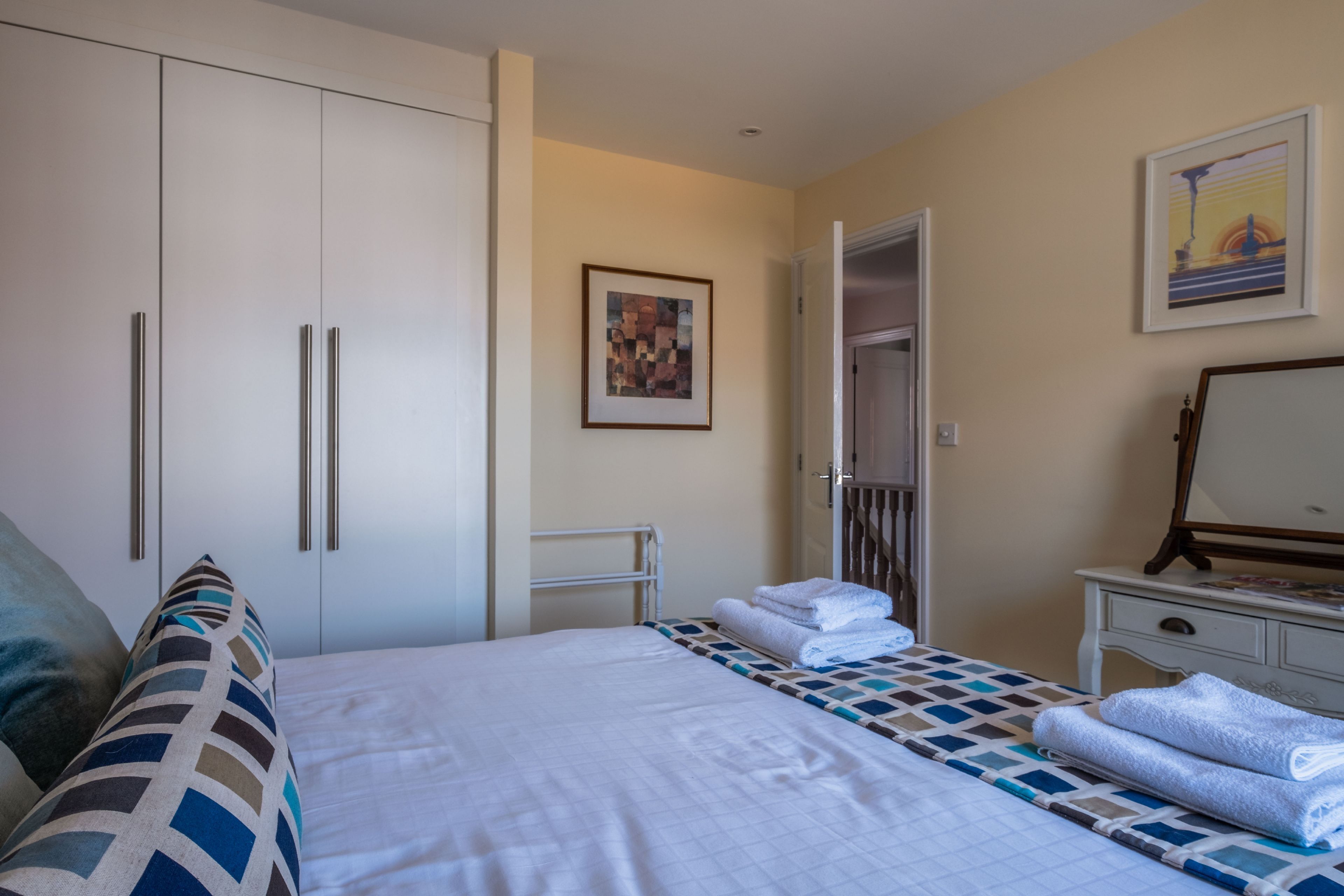 Une chambre d’hôtel comprenant un lit, une armoire, une table de chevet avec un miroir et une porte donnant sur une autre pièce.