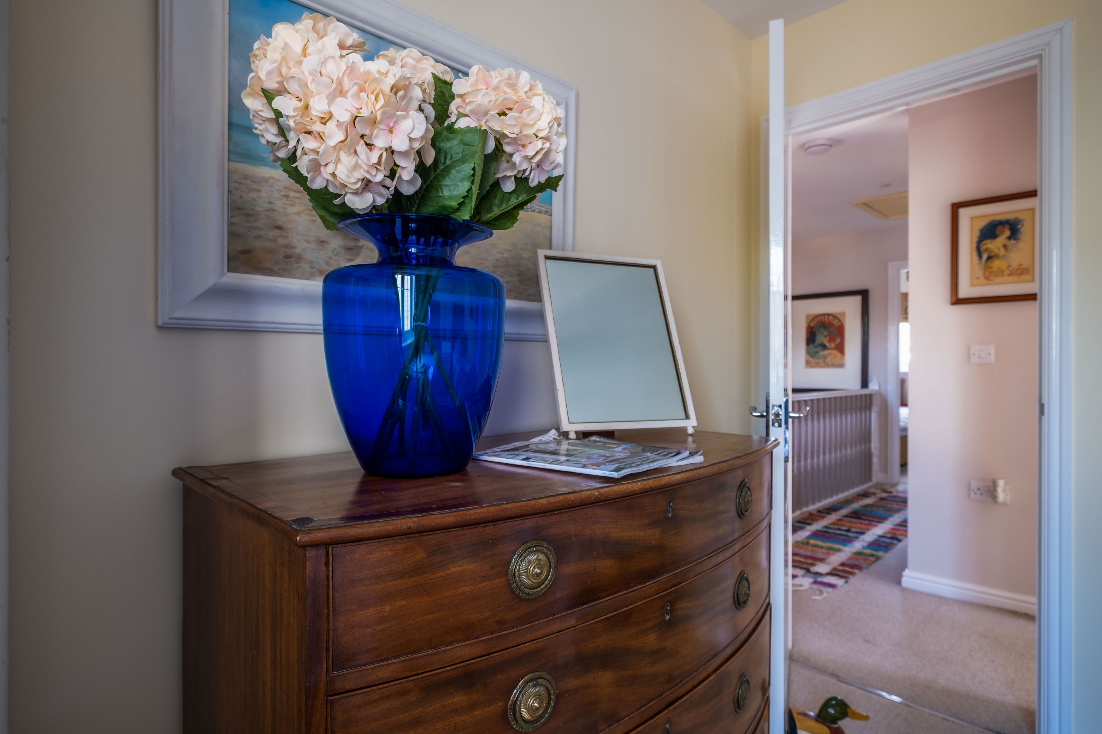 A wooden dresser with a blue vase and a laptop.