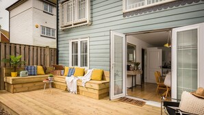 A wooden deck with a sofa and a chair, a small table, and a potted plant. - Rye Bay House -  a cottage that sleeps 8 guests  in 4 bedrooms (Rye)