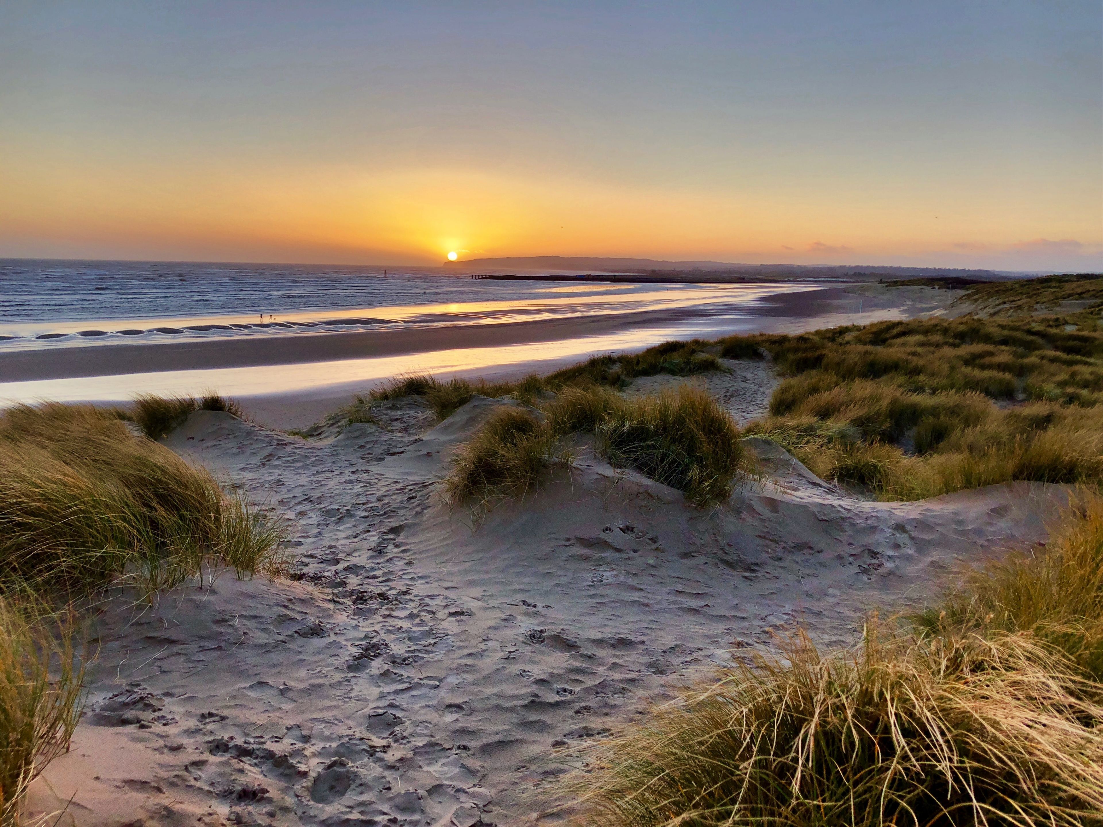 Une plage avec des dunes de sable et un coucher de soleil en arrière-plan.