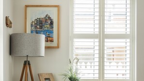 Una sala de estar acogedora con un sofá azul, una lámpara de pie, un cuadro enmarcado, una planta en maceta y una mesita con objetos decorativos.