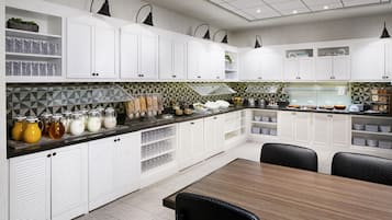 A modern kitchen with white cabinets, a black countertop, and a dining area with a wooden table and chairs.