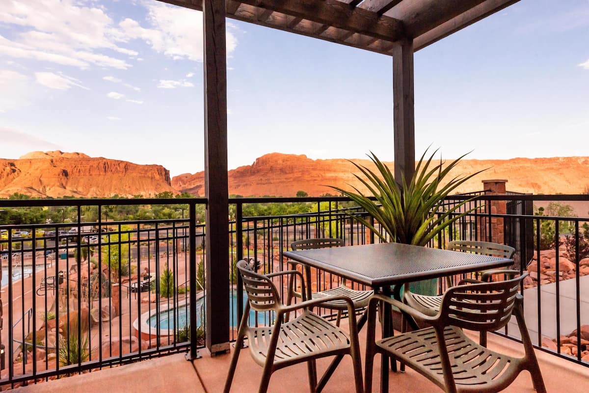 A covered outdoor area with a table and chairs, a pool, and a view of red rock formations.