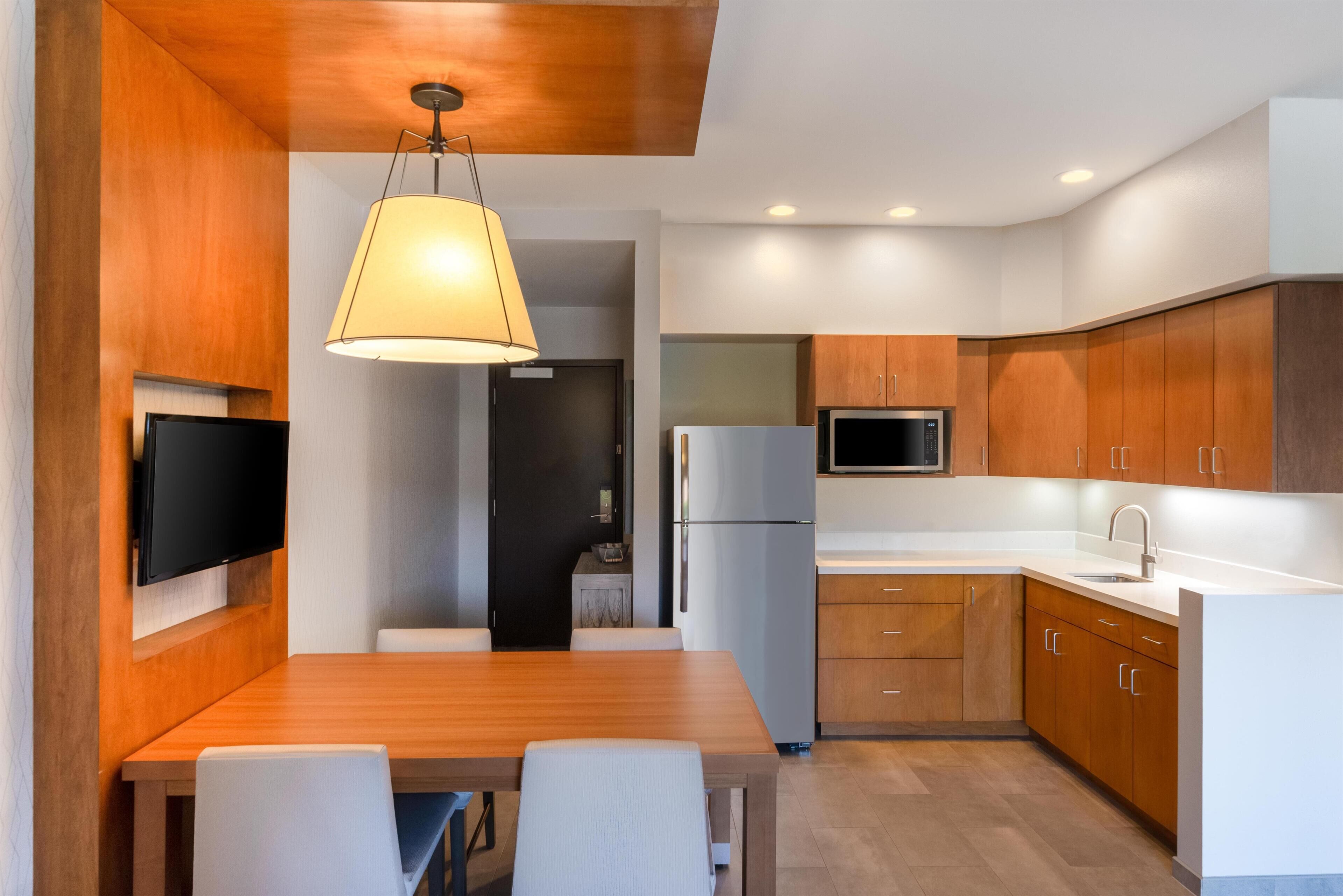 A modern kitchen with wooden cabinets, a built-in microwave, and a dining area with a table and chairs.