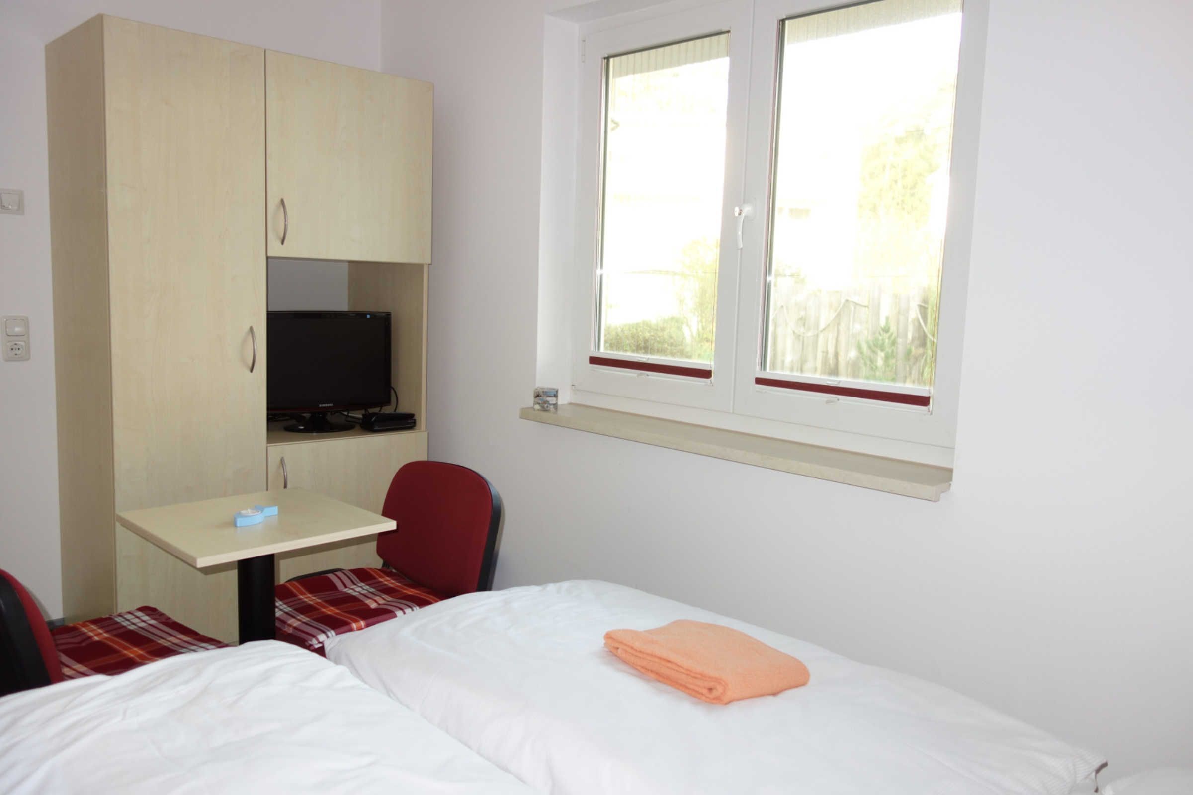 Une petite pièce comprenant un lit, un bureau avec un ordinateur, une chaise et une fenêtre.