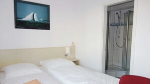 Habitación de hotel con cama, una mesita, una silla roja, ducha y un cuadro en la pared.
