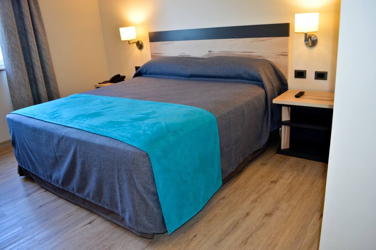 A hotel room with a bed, bedside tables, a nightstand, a lamp, and a telephone.