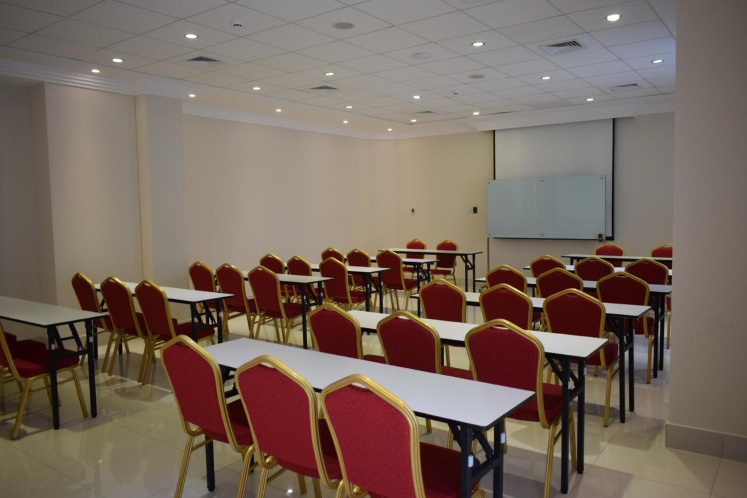 A conference room with rows of tables and chairs, a whiteboard, and a projector screen.