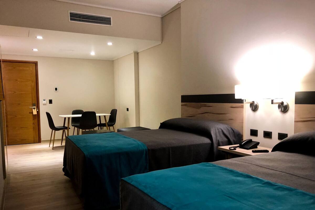 A hotel room with two beds, a desk, a chair, a phone, and a wall-mounted light.