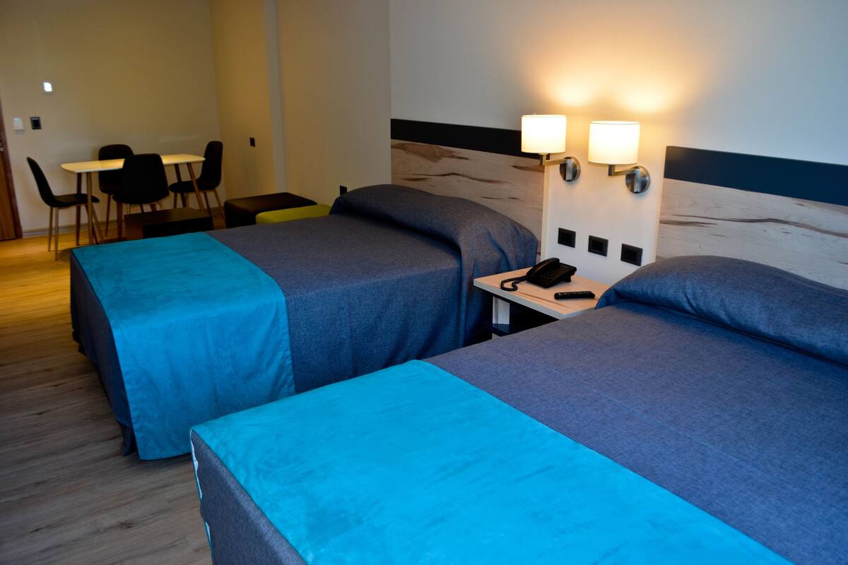 A hotel room with two beds, a desk with a telephone, and a dining area with chairs and a table.