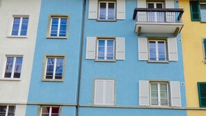 A multi-story building with a flat facade, featuring a series of windows with shutters, a visible entrance, and a staircase leading to the entrance. - Top modern 2-bedroom penthouse apartment in Bern - Beautiful flat roof in Berne City (Bern)