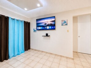 Una habitación con un televisor de pantalla plana montado en la pared, una puerta y piso con baldosas.