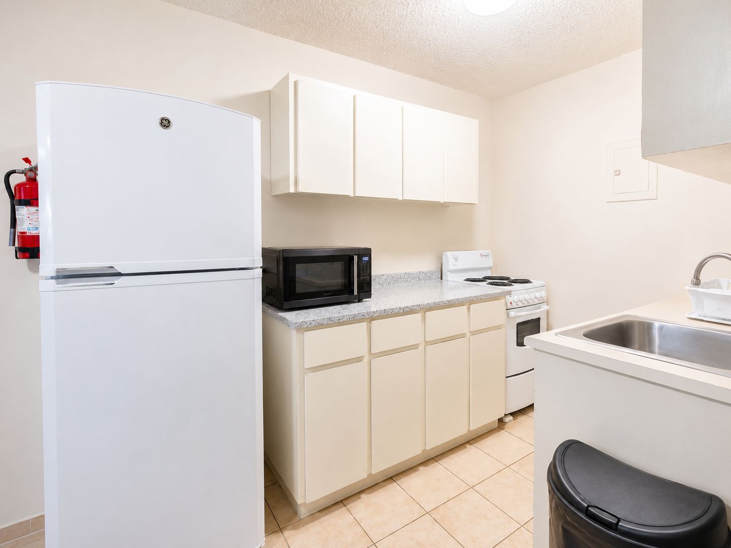 A compact kitchen with a white refrigerator, a microwave, a stove, and a sink.
