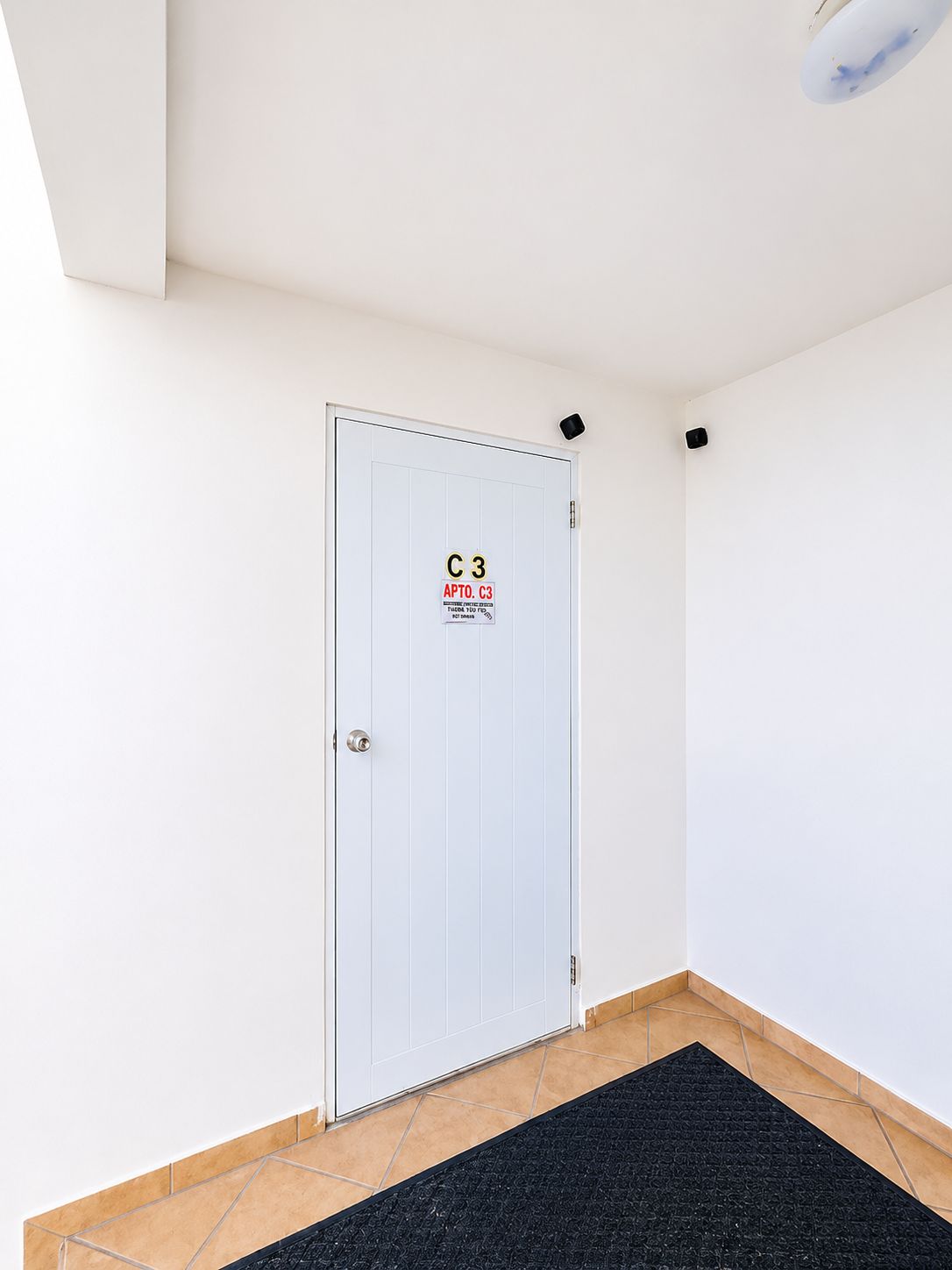 Una puerta blanca con un letrero de seguridad, un felpudo negro y un piso de baldosas.
