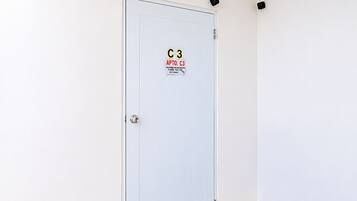 Una puerta blanca con un letrero de seguridad, un felpudo negro y un piso de baldosas.