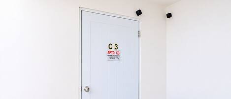 A white door with a security sign, a black doormat, and a tiled floor.