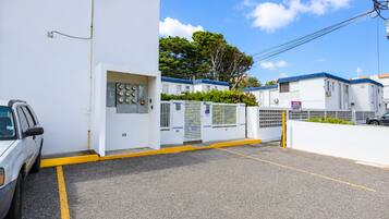 A parking area with a white building, a gated entrance, and a vehicle.