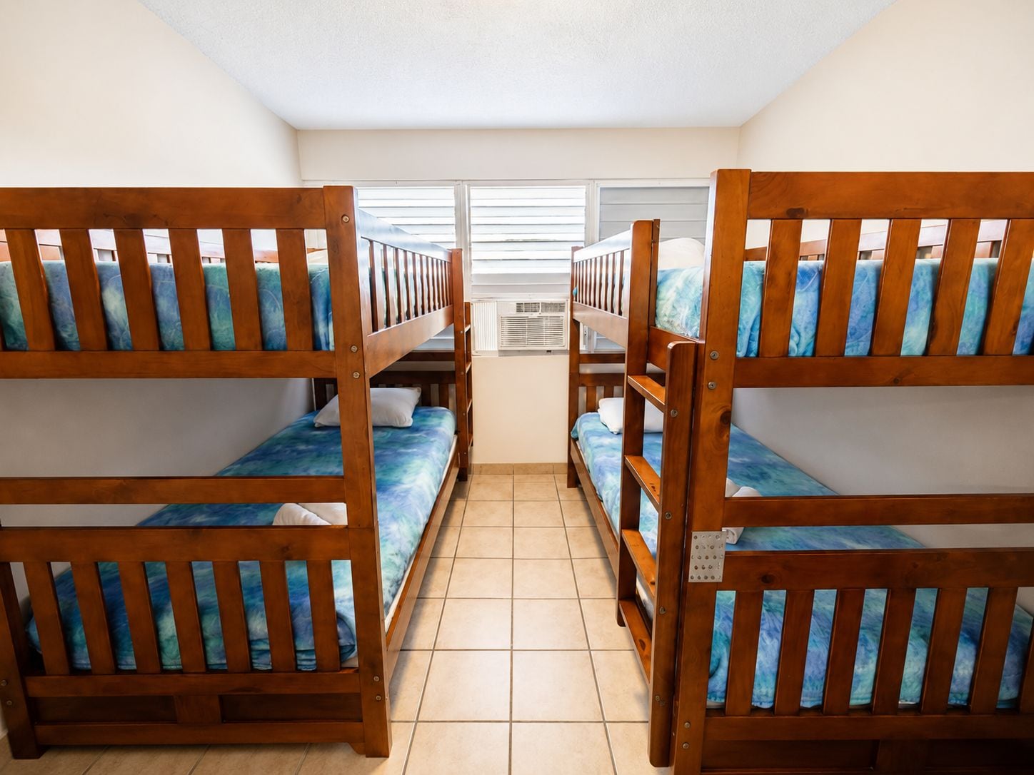 A room with bunk beds, a window with blinds, and an air conditioning unit.