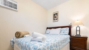 A bedroom with a bed, a nightstand, a lamp, and a wall-mounted air conditioner. - Montones Beach Apartment C-3 (Isabela)