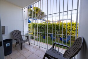 A balcony with two chairs, a trash bin, and a view of a garden and buildings. - Montones Beach Apartment C-3 (Isabela)
