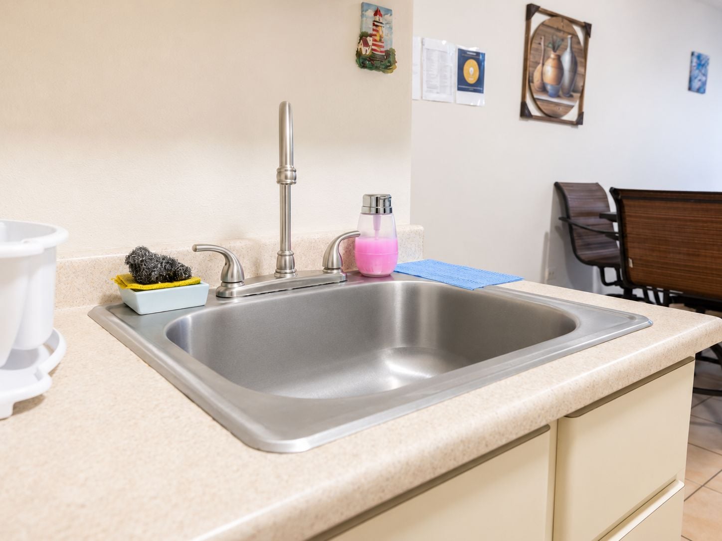 A kitchen with a stainless steel sink, a white coffee maker, and a small dish rack with cleaning supplies.