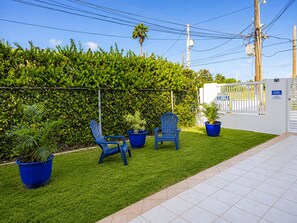 A patio area with a neatly trimmed hedge, two blue chairs, and potted plants. - Montones Beach Apartment C-3 (Isabela)