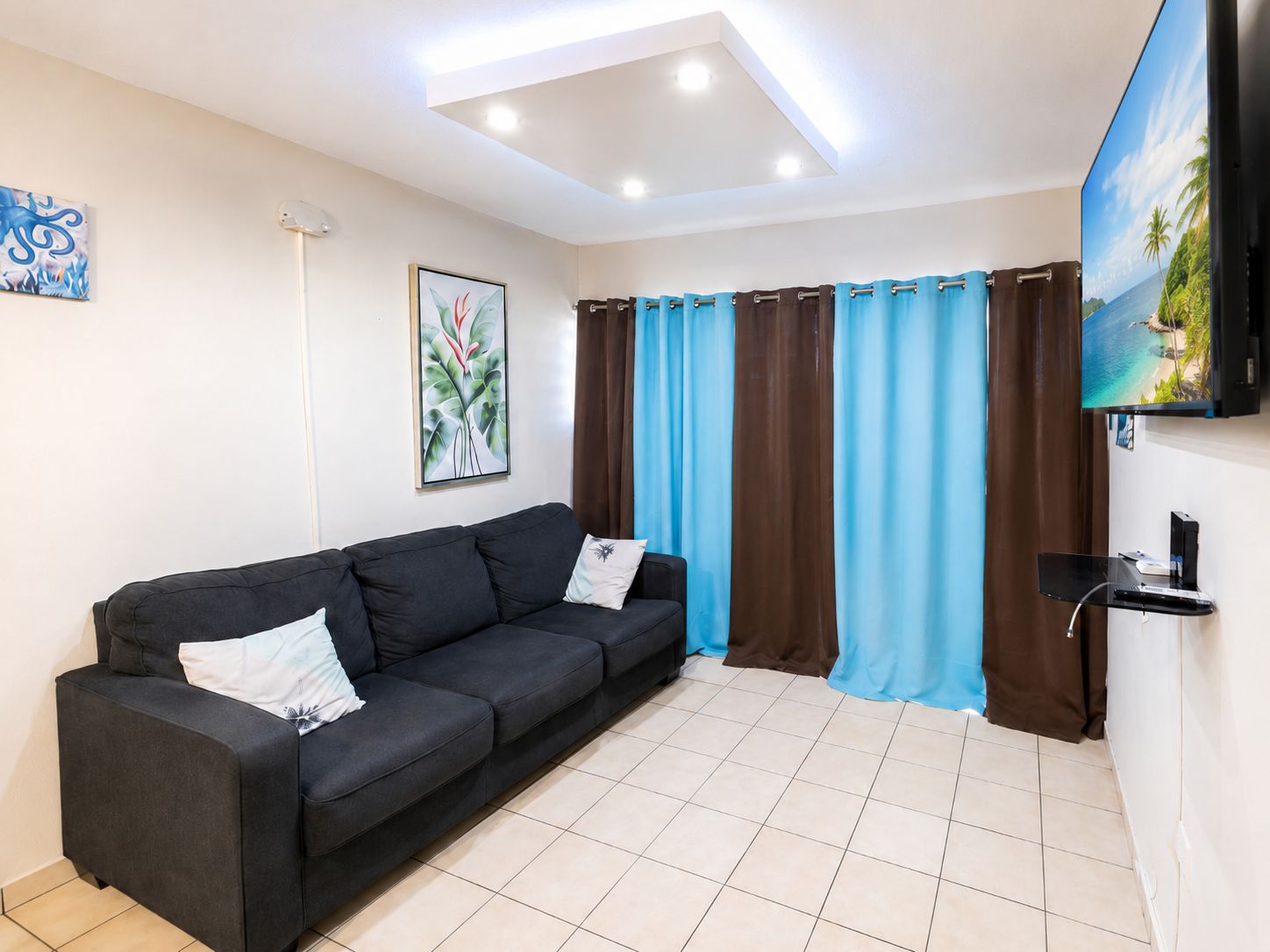 Ein modernes Wohnzimmer mit einem schwarzen Sofa, einem Wand-Fernseher und einer Deckenleuchte.