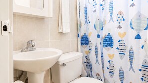A bathroom with a toilet, sink, and shower curtain with a fish pattern. - Montones Beach Apartment C-3 (Isabela)
