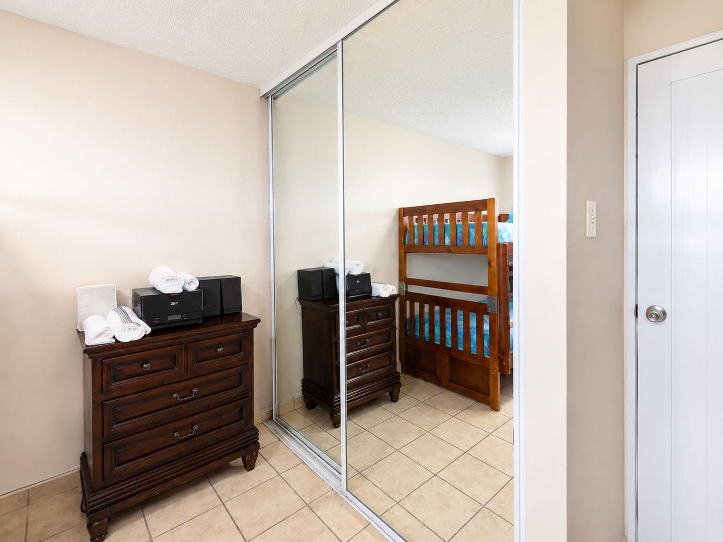 A hotel room with a large mirror, wooden dresser, and a bunk bed.