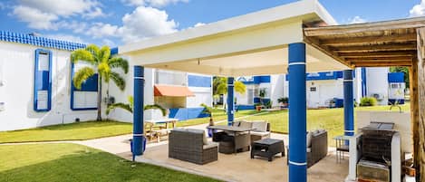 A covered outdoor area with a barbecue, seating, and a view of a building with blue and white exterior.