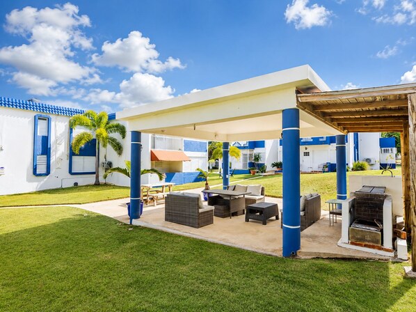 A covered outdoor area with a barbecue, seating, and a view of a building with blue and white exterior.