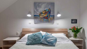 Camera da letto con un letto, due comodini, un tavolino e un quadro appeso al muro, con un vaso di fiori.