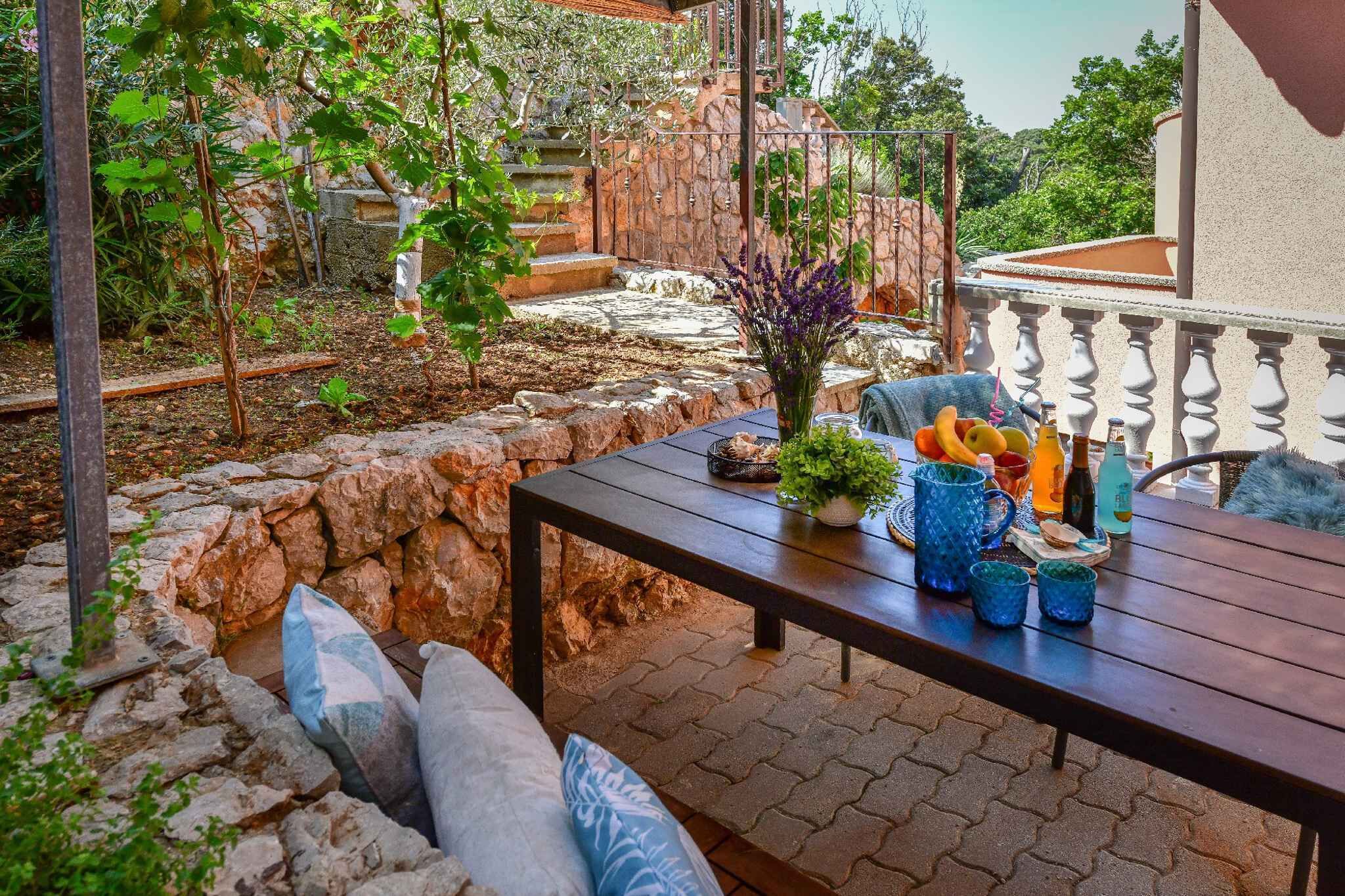 An outdoor patio with a stone wall, a wooden table with drinks and snacks, and a view of a stone staircase and greenery.