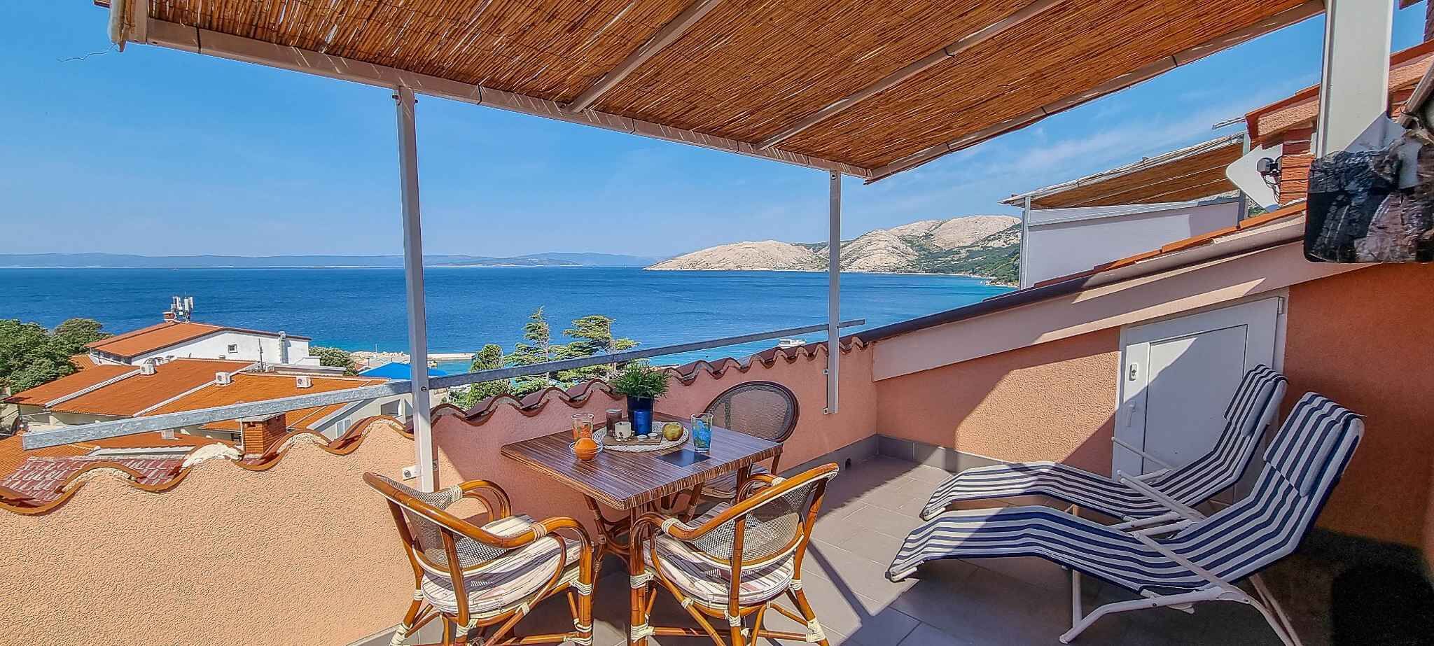 A terrace with a table and chairs overlooking a coastal view.