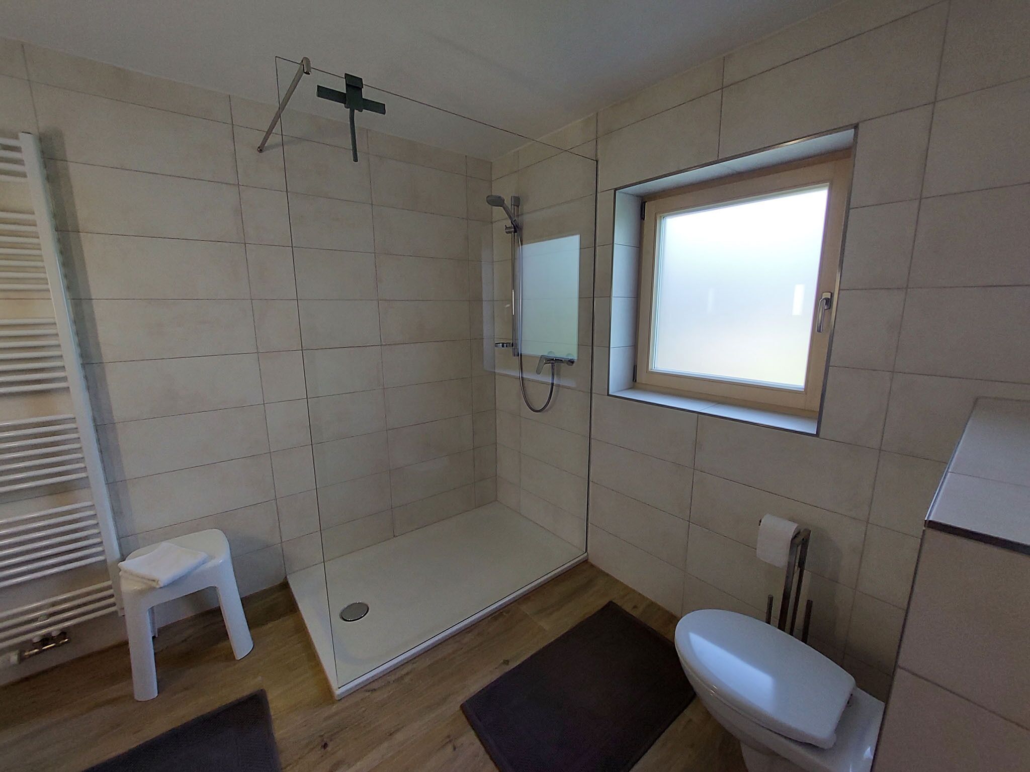 Een moderne badkamer met een douche, toilet en een klein krukje.