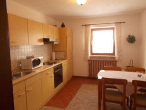A compact kitchen with wooden cabinets, a microwave, a stove, and a dining area with a table and chairs.